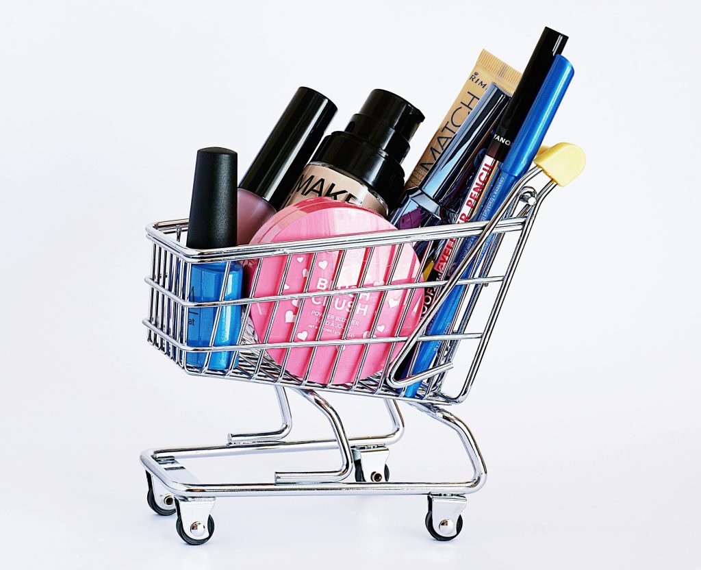 pexels-photo-2536965-2536965 Miniature shopping cart filled with a variety of cosmetics on a white background.